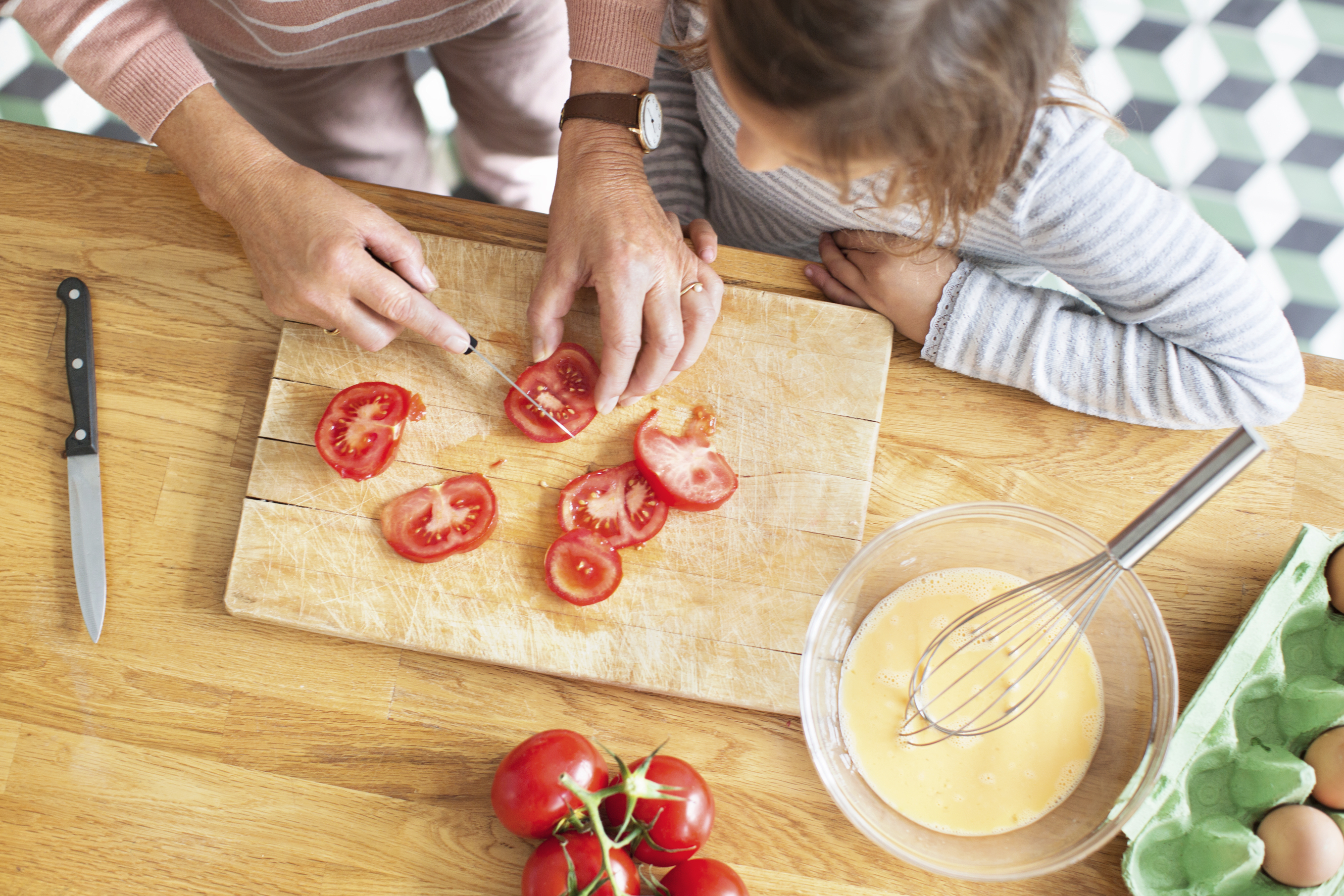 Woman cutting tomatoes while a young child watches.