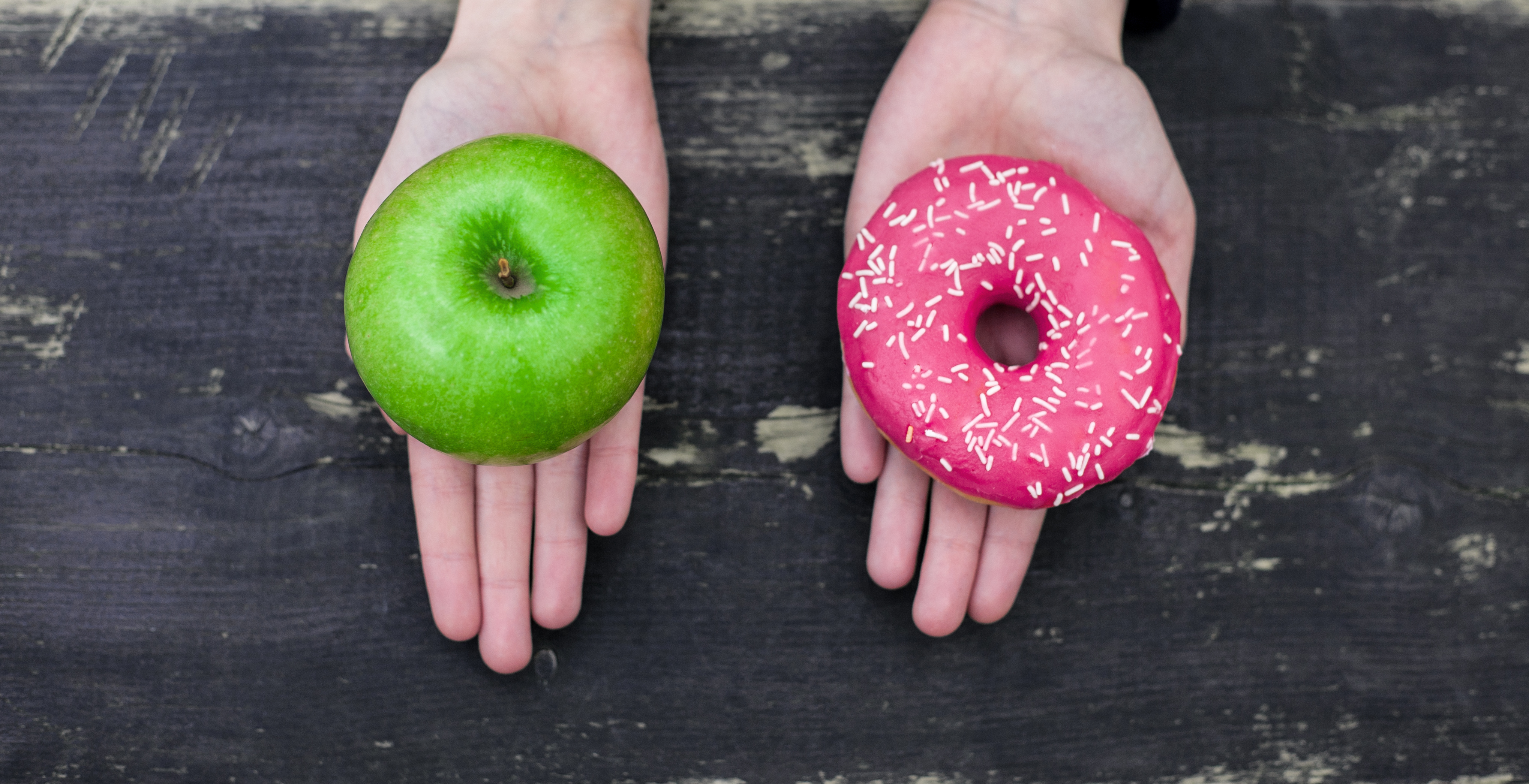 Two hands open holding an apple in one and a donut in the other.