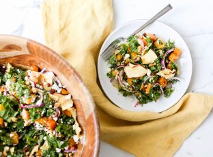 A salad bowl full of Autumn Kale Salad with butternut squash, hazelnuts and apple chips.