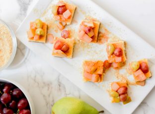 Cheesecake Bites garnished with white wine sautéed pears and grapes on a serving platter.